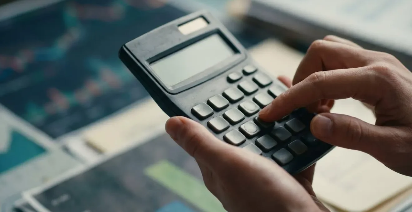 Gros plan sur des mains tenant une calculatrice avec des documents financiers flous en arrière-plan